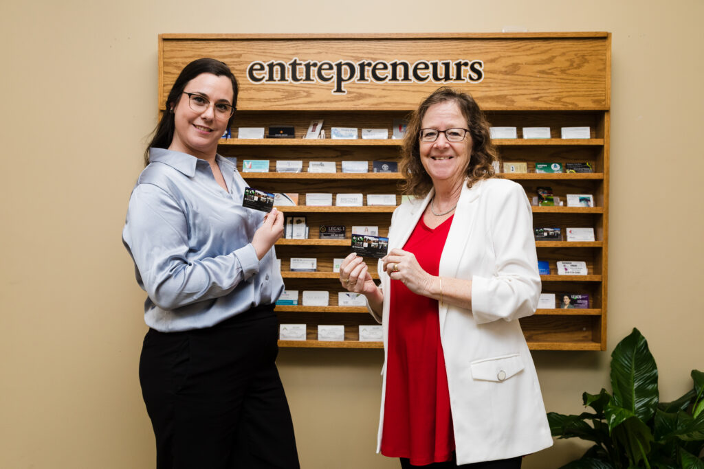 EBRC staff smiling in front of the entrepreneurs business card rack at Elgin Business Resource Centre in St. Thomas, Ontario
